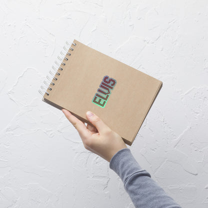 A hand holding a brown kraft paper spiral notebook with the name 'ELVIS' printed on the cover in a colorful, glittery font, set against a textured white wall.